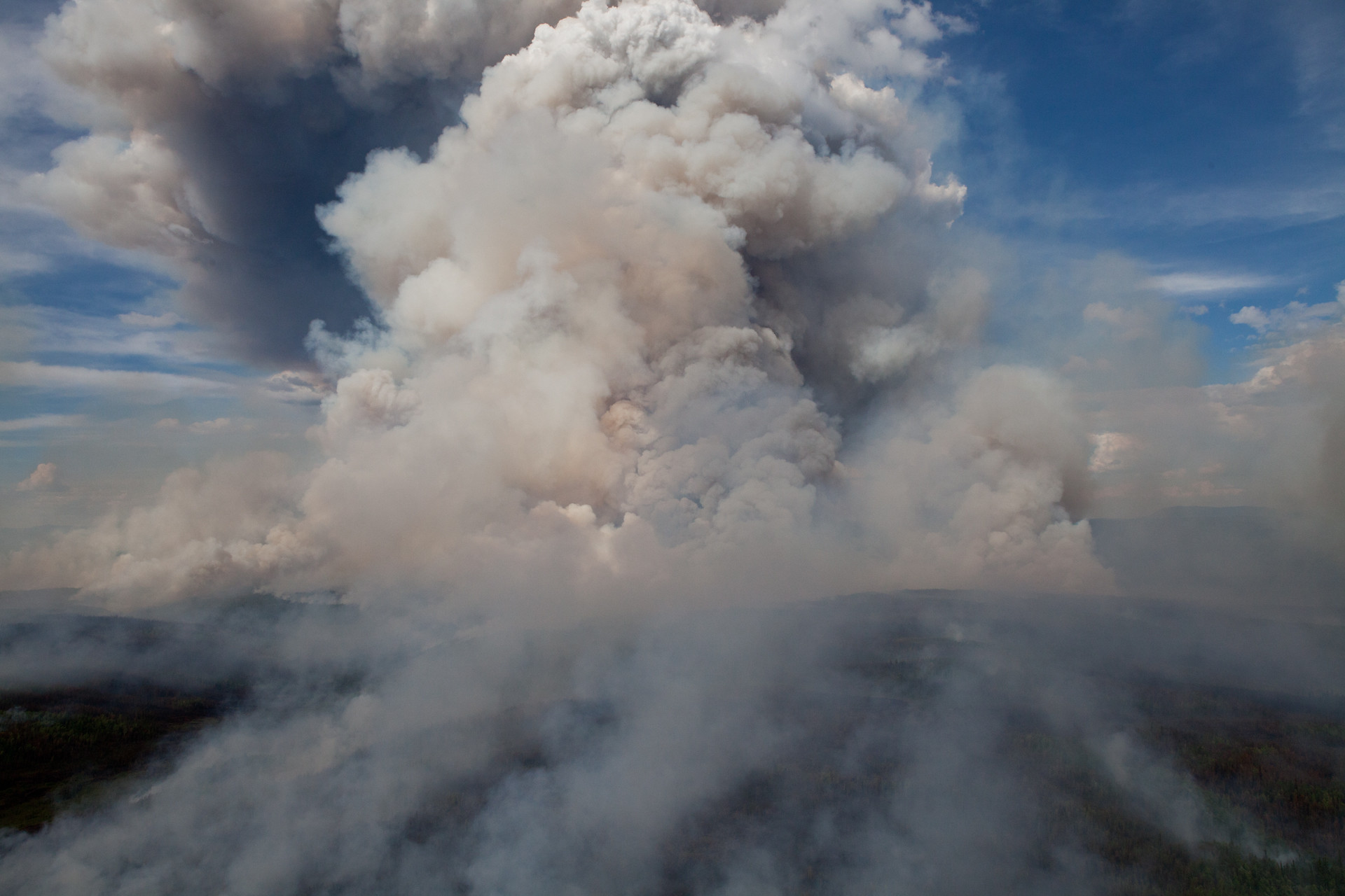 A large smoke column ascends over the Alaskan tundra.